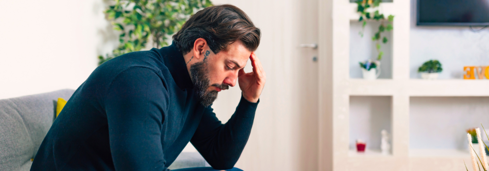 Man sitting on a sofa with his head in his hand, showing signs of emotional distress or mental strain.