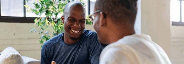 Two men smiling and laughing together, symbolising positive social interactions and the importance of mental health support in the workplace.