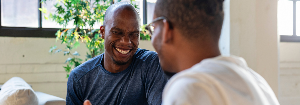 Two men smiling and laughing together, symbolising positive social interactions and the importance of mental health support in the workplace.