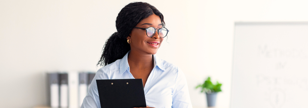 Smiling early-career mental health professional holding a clipboard, reflecting confidence and support at the beginning of her clinical journey.