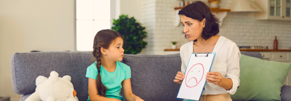 Child and CAMHS clinician sitting on a sofa during a therapy session, using visual tools to support emotional expression.